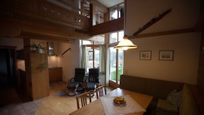 A spacious living area with a wooden dining table, a sofa, and a staircase leading to an upper level.