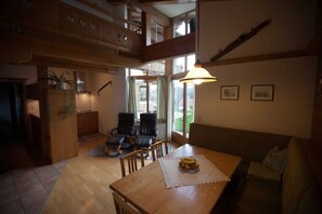 A spacious living area with a wooden dining table, a sofa, and a staircase leading to an upper level.