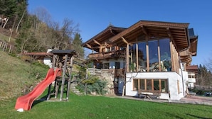A chalet-style building with a wooden exterior, a large glass window, and a red slide in the foreground.