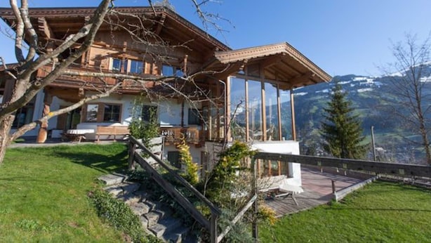 A traditional chalet with a wooden facade, a balcony, and a view of mountains in the background.