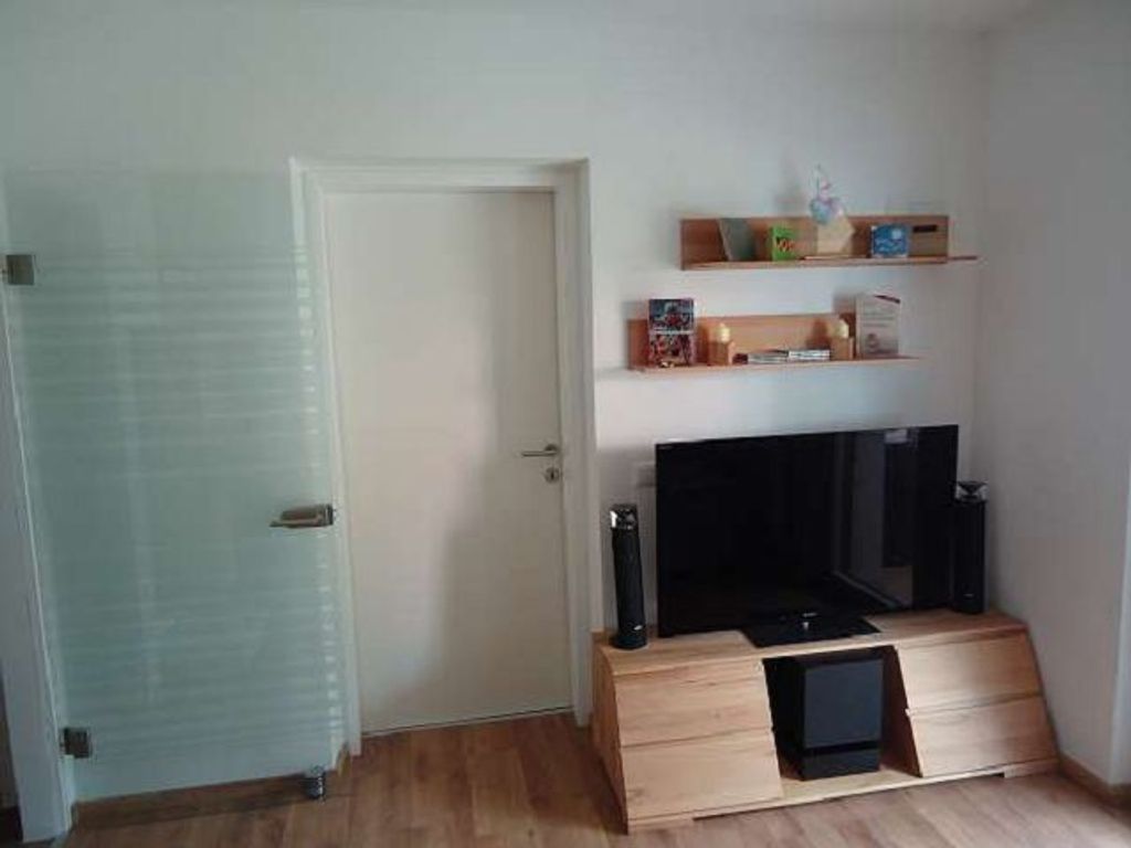 Ein Zimmer mit einem Holzkasten, einem Fernseher und Regalen mit Gegenständen.