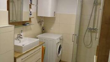 Une salle de bain équipée d’un lavabo, d’un miroir, d’un meuble de rangement, d’une machine à laver et d’une douche.