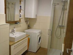 Une salle de bain équipée d’un lavabo, d’un miroir, d’un meuble de rangement, d’une machine à laver et d’une douche.