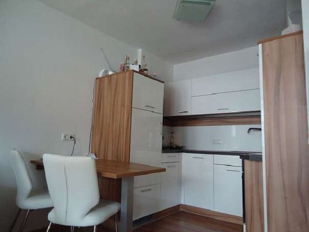 A compact kitchen with white cabinets, a wooden countertop, and a white chair.