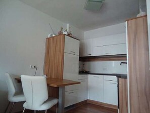 Eine kleine Küche mit weißen Schränken, einer Holz Arbeitsplatte und einem weißen Stuhl.
