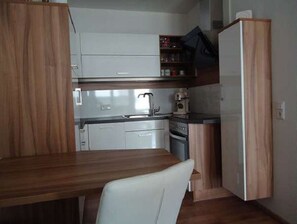 Une cuisine compacte avec des meubles blancs, un plan de travail en bois et un four encastré.