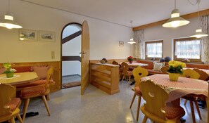 A cozy dining area with wooden furniture, a large open door leading to a balcony, and a window with floral curtains.