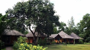 A row of thatched-roof cottages with a paved pathway leading to them, surrounded by lush greenery and yellow flowers. - Payam Cottage Resort (Ranong)
