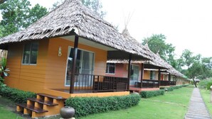 A bungalow with a thatched roof, a covered porch, and a small garden area with a pathway. - Payam Cottage Resort (Ranong)