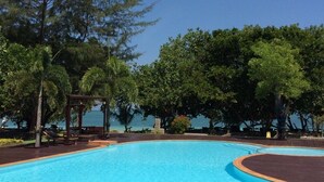 A clear blue pool with a wooden deck surrounding it, trees in the background, and a clear sky. - Payam Cottage Resort (Ranong)