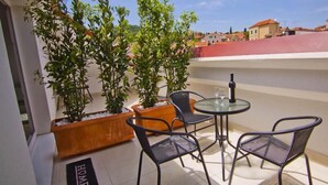 Un balcón con mesa y sillas, plantas en macetas y vistas a edificios.
