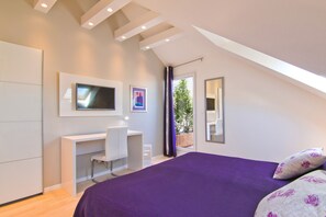 A bedroom with a bed, a desk, a chair, a TV, and a window with a view of greenery. - Laura Lux Suites (Split)
