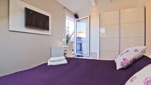 Una habitación de hotel moderna con una cama grande, un televisor de pantalla plana montado en la pared, un escritorio con una silla y una puerta corredera que da a un balcón.