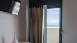 Habitación de hotel con cama, una mesita, un florero y vista al mar a través de una puerta corrediza.