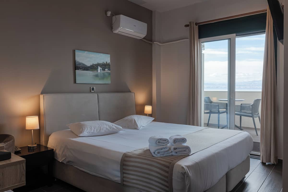 A hotel room with a large bed, a view of the outdoors, and a balcony with chairs.
