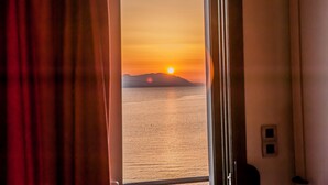 Habitación con vista a un atardecer sobre el agua, cortinas entreabiertas y un interruptor de luz pequeño fijado a la pared.