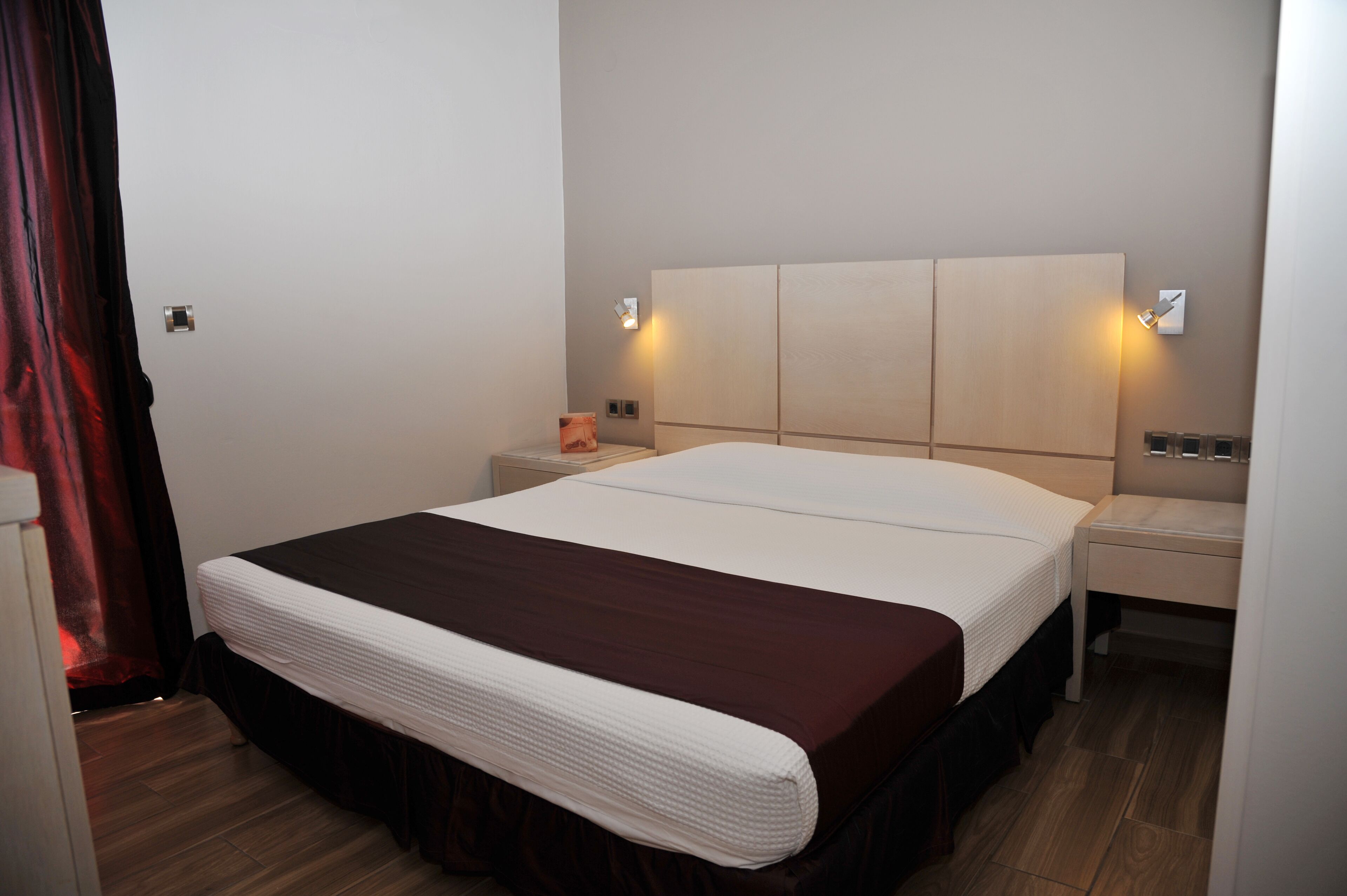 Een hotelkamer met een groot bed, twee nachtkastjes en een wandlamp.