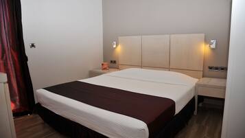 Een hotelkamer met een groot bed, twee nachtkastjes en een wandlamp.