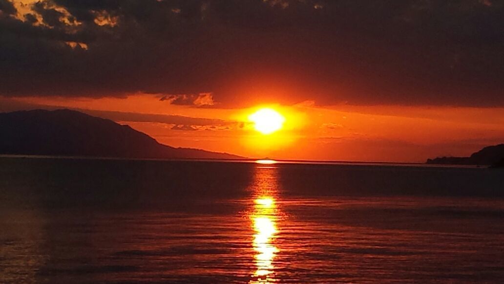A sunset over a calm body of water with mountains in the background.