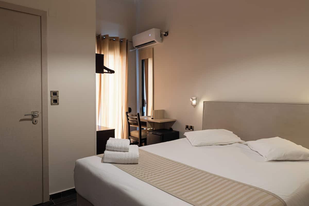 A hotel room with a bed, a desk, a chair, and an air conditioning unit.