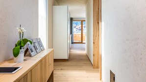 A narrow hallway with wooden flooring, a white cabinet with a tablet and framed photos, and a potted plant. - Holztau, Pfunds, Austria (Pfunds)