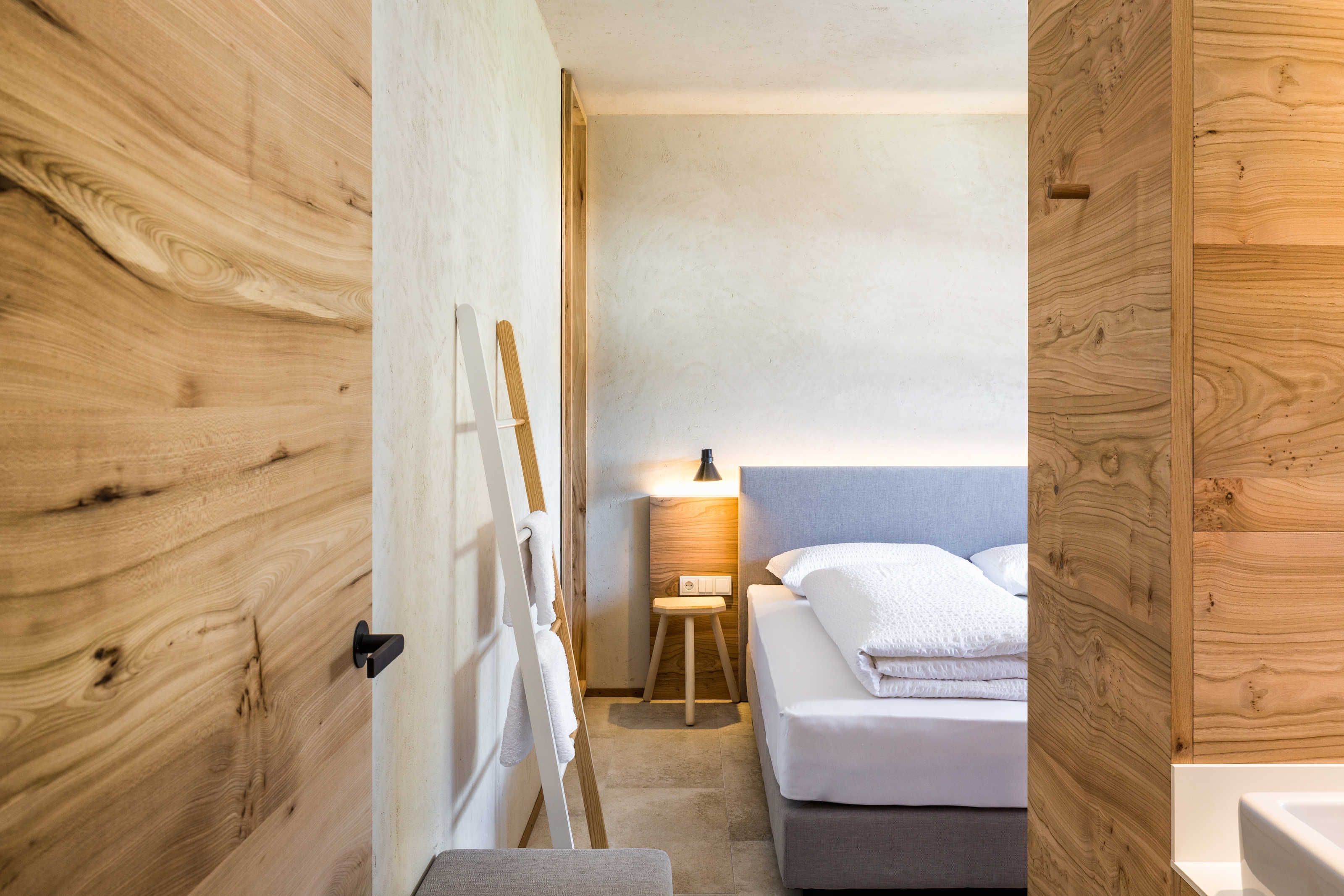 A small, compact room with a bed, a nightstand, a lamp, and a wooden door.