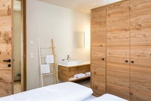 A hotel room with a wooden wardrobe, a white bed, a wooden vanity with a sink, and a towel rack. - Holztau, Pfunds, Austria (Pfunds)