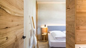 A small, compact room with a bed, a nightstand, a lamp, and a wooden door. - Holztau, Pfunds, Austria (Pfunds)