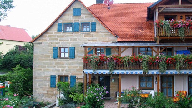 En toetages stengul bygning med en balkon pyntet med blomster, en træterrasse og et rødt tegltag.