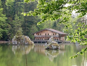 A wooden lodge with a balcony, situated by a calm lake with two prominent rocks in the foreground.