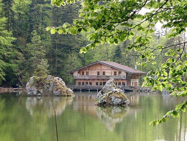 A wooden lodge with a balcony, situated by a calm lake with two prominent rocks in the foreground.
