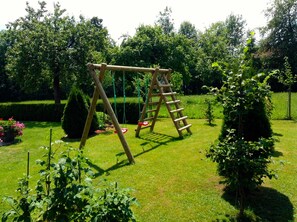 A wooden swing set in a well-maintained garden with hedges and flowering plants.