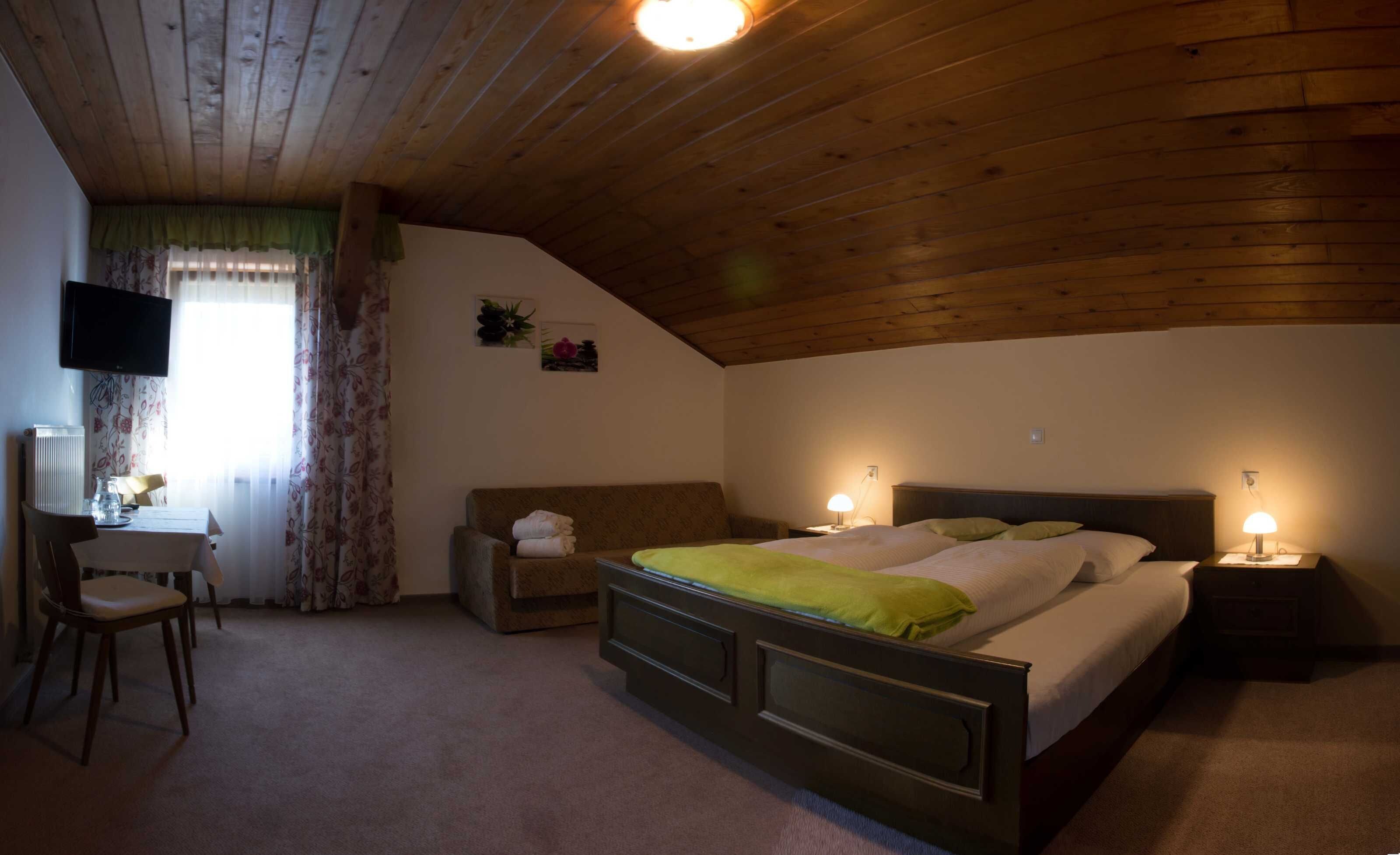 Ein Schlafzimmer mit Bett, Nachttischlampen, einem Sessel, einem Tisch und einem Fernseher.