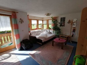 A room with a bed, a small table, a chair, a plant, and a window with curtains.
