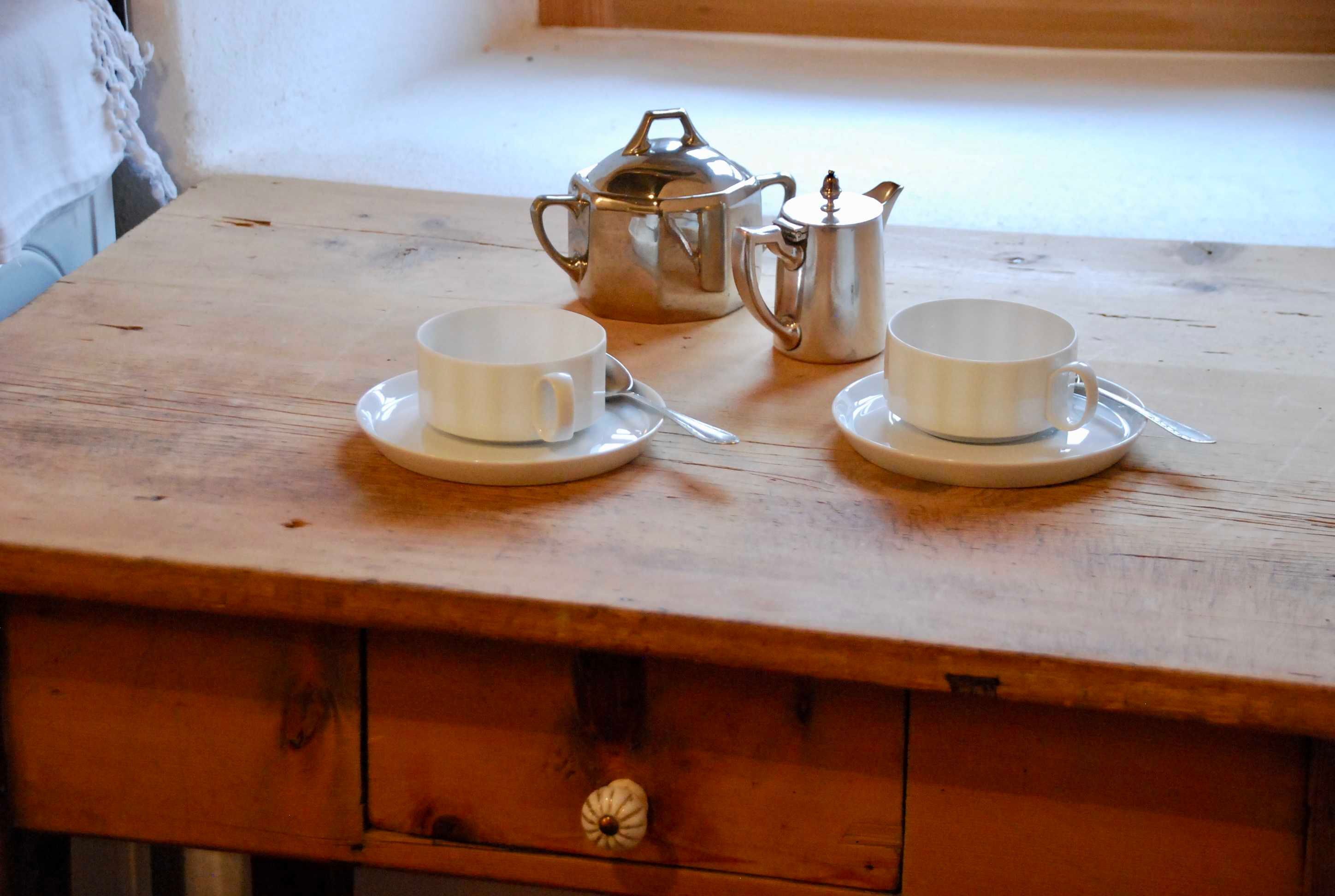 A wooden table with two white cups and a silver teapot on it.