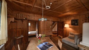 Een houten blokhut van binnen, met een eettafel, stoelen, een bank, een lamp en een trap.