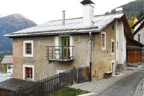 A traditional stone building with a balcony, a wooden fence, and a mountain backdrop.