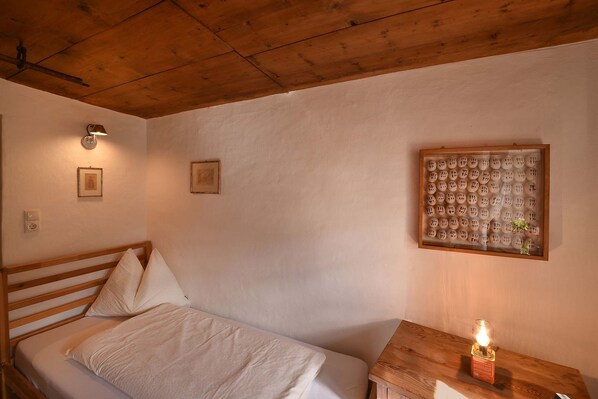 A bedroom with a wooden bed, a nightstand with a candle, and a wall-mounted light fixture. - House 59 Stelvio, Italy (Stilfs)