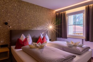 Une chambre d’hôtel avec un mur en granit, un lit avec une literie à carreaux, des oreillers rouges et blancs, et une fenêtre avec des rideaux.