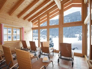 A wooden interior with large windows, wicker chairs, and a view of snow-covered mountains.