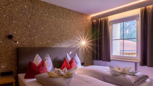 Hotelkamer met een wand van graniet, een bed met geruit beddengoed, rode en witte kussens, en een raam met gordijnen.