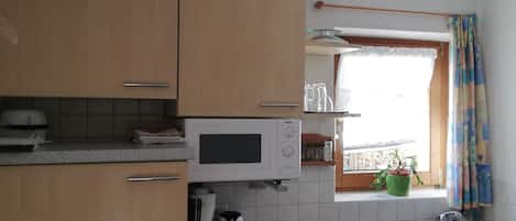 A kitchen with wooden cabinets, a microwave, a stove, and a window with curtains.
