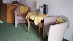 A small room with a television on a stand, a table with a yellow tablecloth, two chairs, and a wall-mounted light fixture. - Künzelspitze DZ#2 - Ritter Anni - Haus Ritter (Schoppernau)