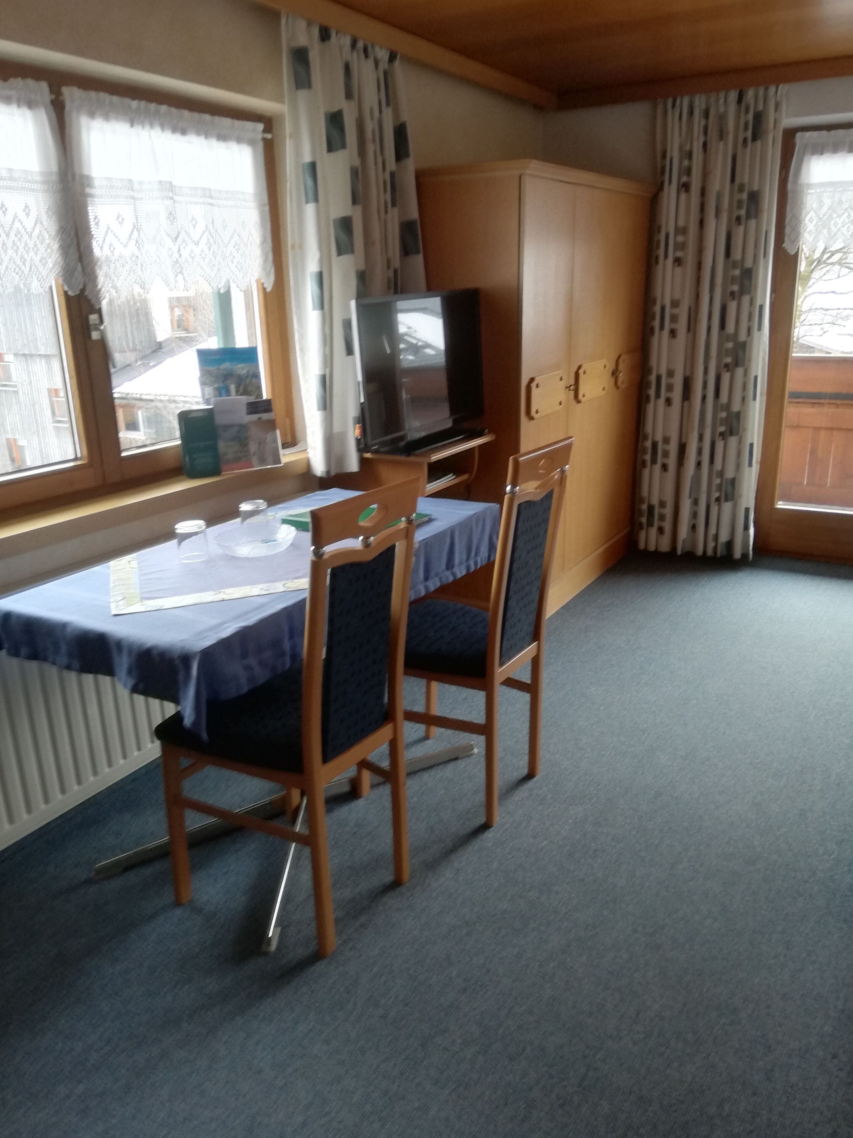 Een kamer met een tafel, stoelen, een televisie en een kledingkast.