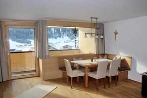 A room with a wooden dining table, white chairs, a bench, a large window with a view of a snowy landscape, and a star decoration. - Künzelspitze DZ#2 - Ritter Anni - Haus Ritter (Schoppernau)