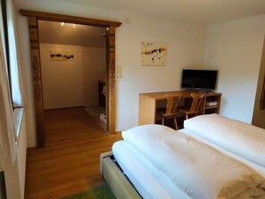 Ein Zimmer mit einem Bett, einem Schreibtisch mit Stuhl, einem Fernseher und einer Tür zu einem anderen Raum.