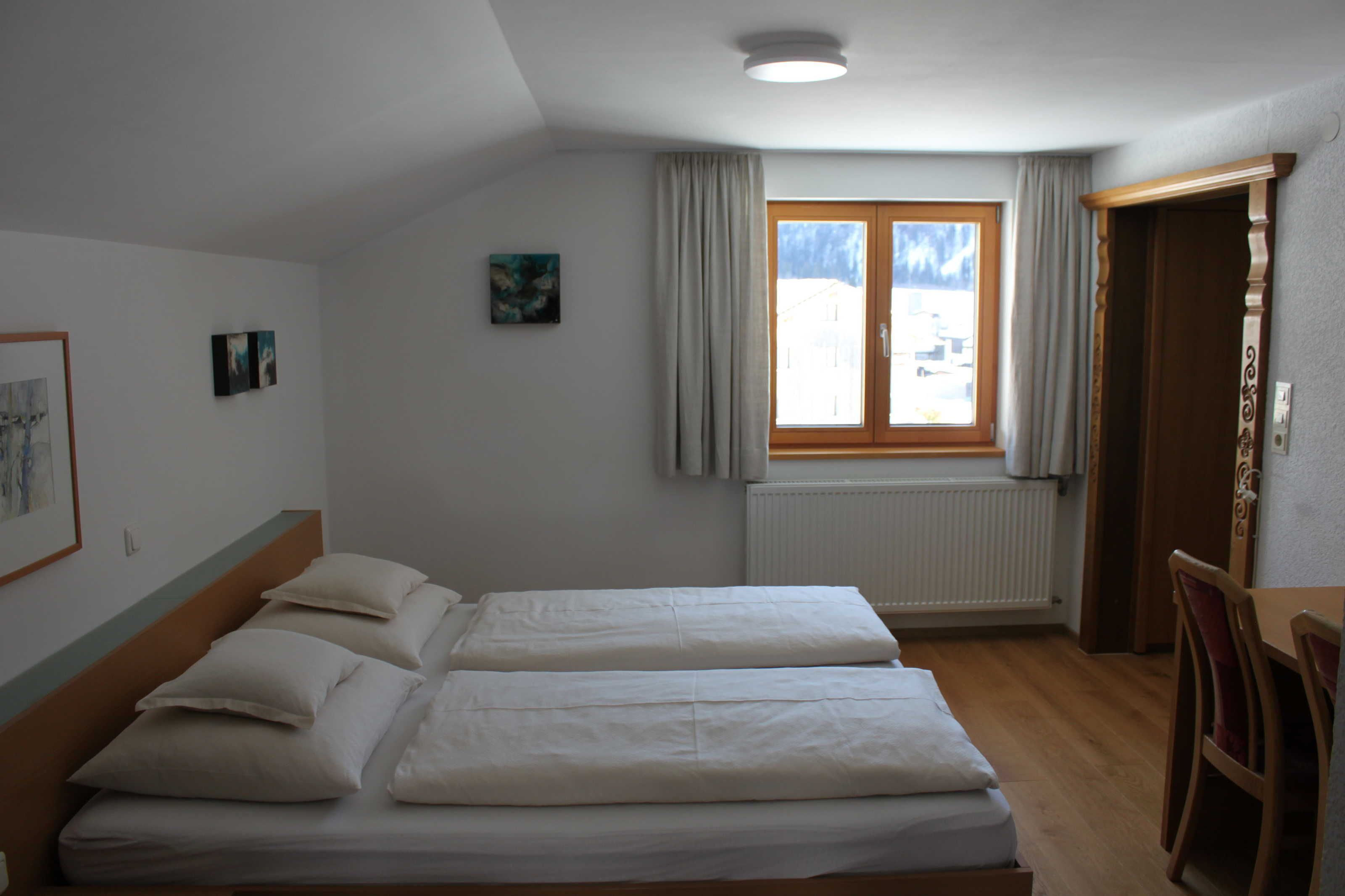 Ein Hotelzimmer mit zwei Betten, einem Fenster mit Vorhängen, einem Heizkörper und einer Tür.