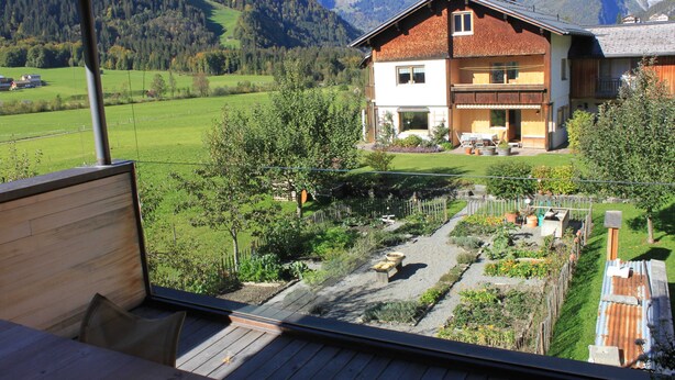Una casa de dos pisos con jardín, terraza de madera y vista a la montaña.