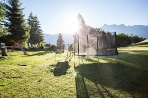 Un trampolín en una zona verde con árboles y montañas al fondo.