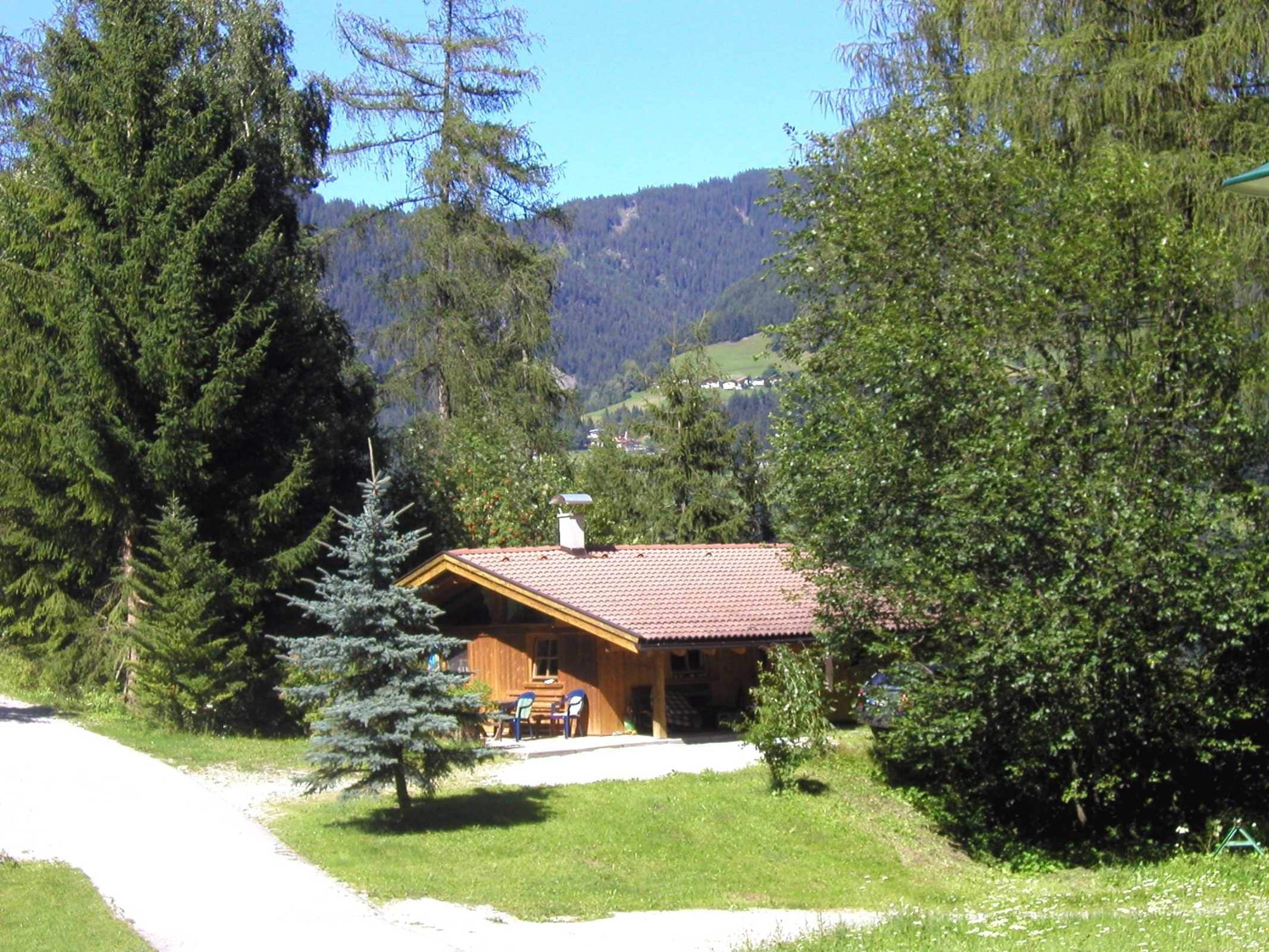 Eine Holzhütte mit rotem Ziegeldach, umgeben von Bäumen und einem klaren Himmel.